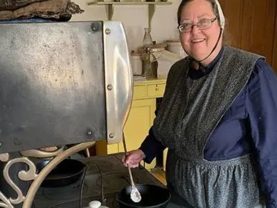 woman in period costume standing in front of wood stove cooking
