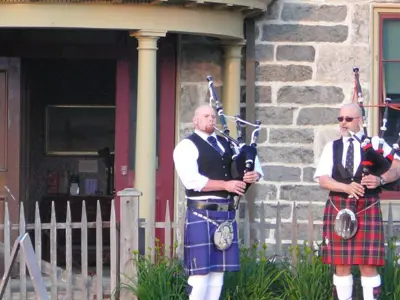two pipers playing in front of McDougall Cottage