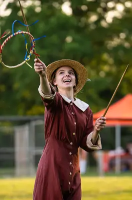 Young woman in period costume using sticks to throw a ribboned hoop