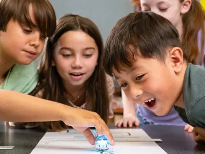 group of young kids watching small round robot on a table