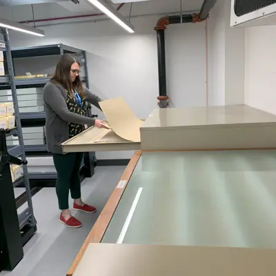 woman pulling large documents out of wide file cabinet