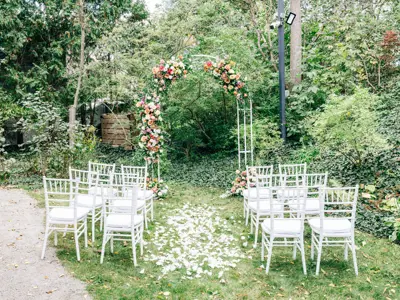 chairs set on either side of an aisle facing an arch covered in flowers