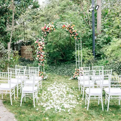 chairs set on either side of an aisle facing an arch covered in flowers
