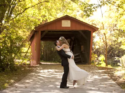 groom picking up and kissing bride in front of covered bridge